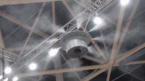 An industrial humidifier sprays water particles around itself at the ceiling of an industrial plant. Shot in motion
