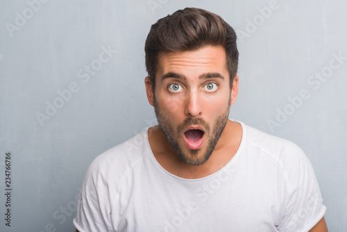Handsome young man over grey grunge wall scared in shock with a surprise face, afraid and excited with fear expression