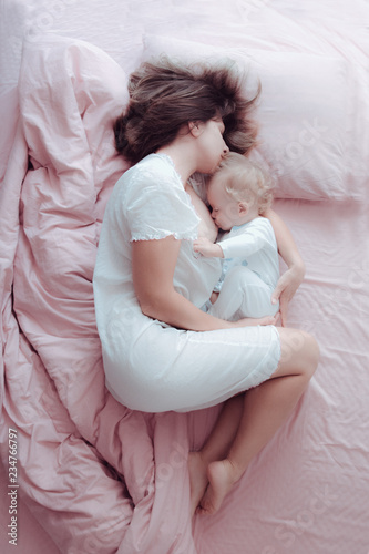 Young mother is breastfeeding a baby lying in bed