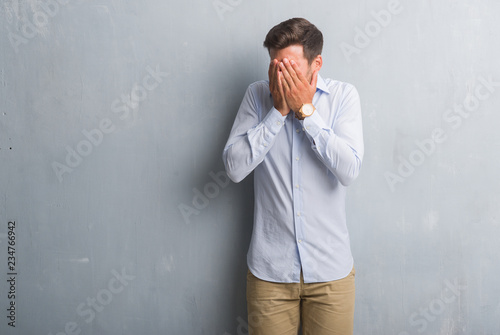 Handsome young business man over grey grunge wall wearing elegant shirt with sad expression covering face with hands while crying. Depression concept. © Krakenimages.com