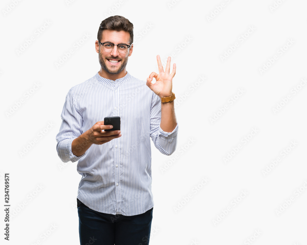 Young handsome man texting using smartphone over isolated background doing ok sign with fingers, excellent symbol