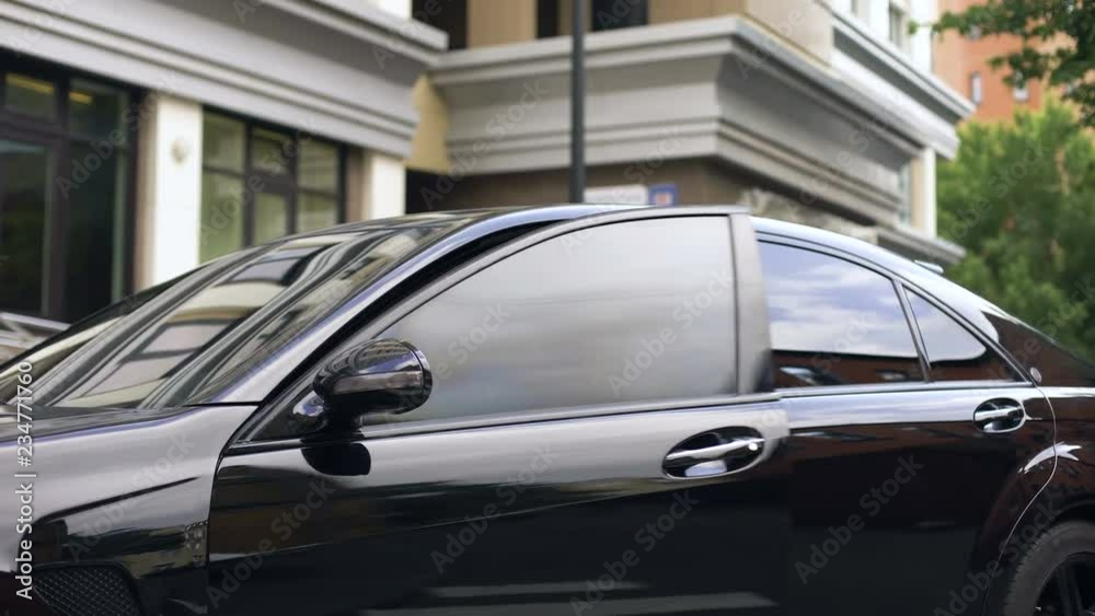 Handsome office worker getting in new luxury car near business center, promotion