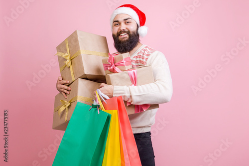 Happy man in Santa's hat holding a lot of Christmas gift boxes with colored packages pressed to him