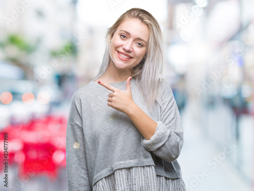 Young blonde woman over isolated background cheerful with a smile of face pointing with hand and finger up to the side with happy and natural expression on face looking at the camera.