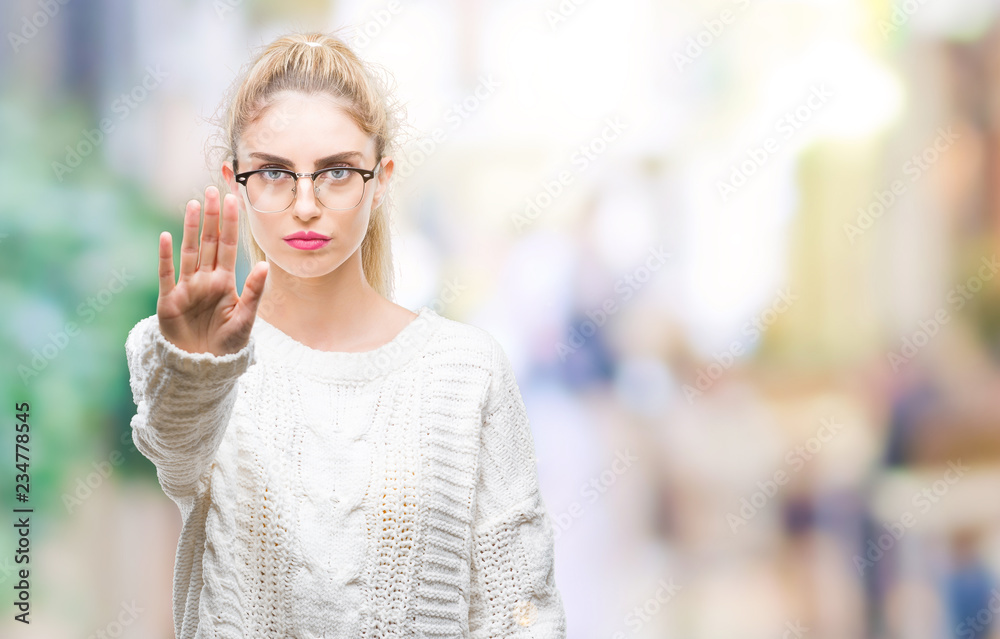 Young beautiful blonde woman wearing glasses over isolated background doing stop sing with palm of the hand. Warning expression with negative and serious gesture on the face.