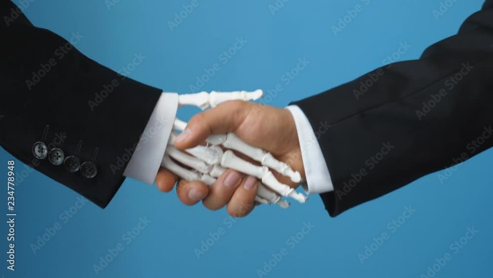 Making a deal with death. Man shakes hand of medical skeleton in suit. Blue background.