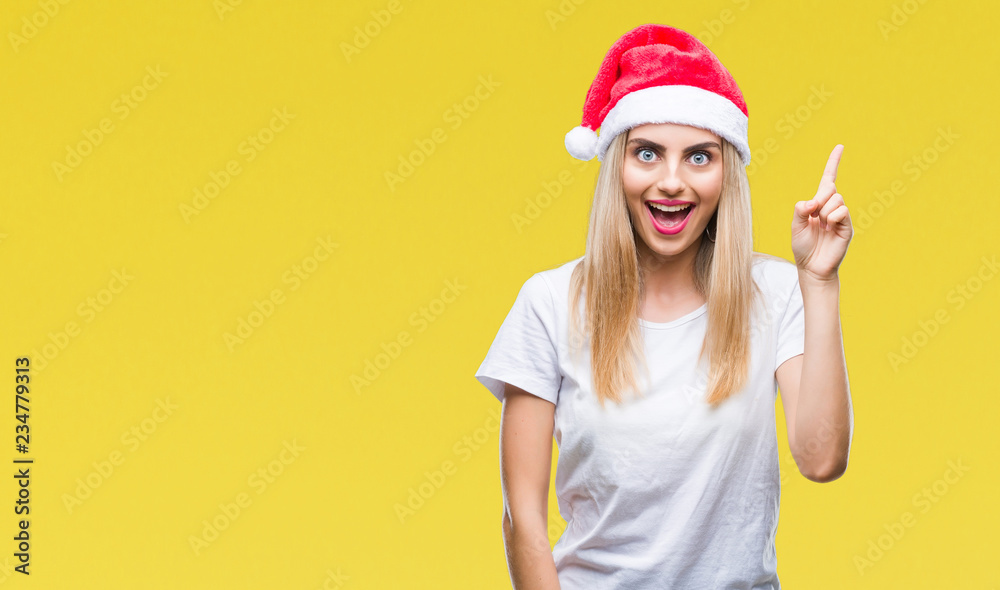 Young beautiful blonde woman christmas hat over isolated background pointing finger up with successful idea. Exited and happy. Number one. Young beautiful blonde woman christmas hat over isolated background pointing finger up with successful idea. Exited and happy. Number one.
