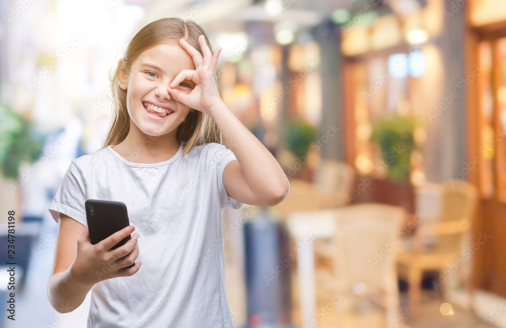 Young beautiful girl sending message texting using smarpthone over isolated background with happy face smiling doing ok sign with hand on eye looking through fingers