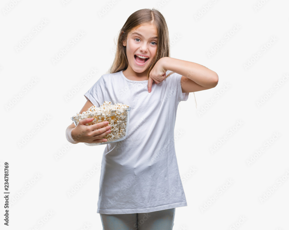Young beautiful girl eating popcorn snack isolated background with surprise face pointing finger to himself Young beautiful girl eating popcorn snack isolated background with surprise face pointing finger to himself