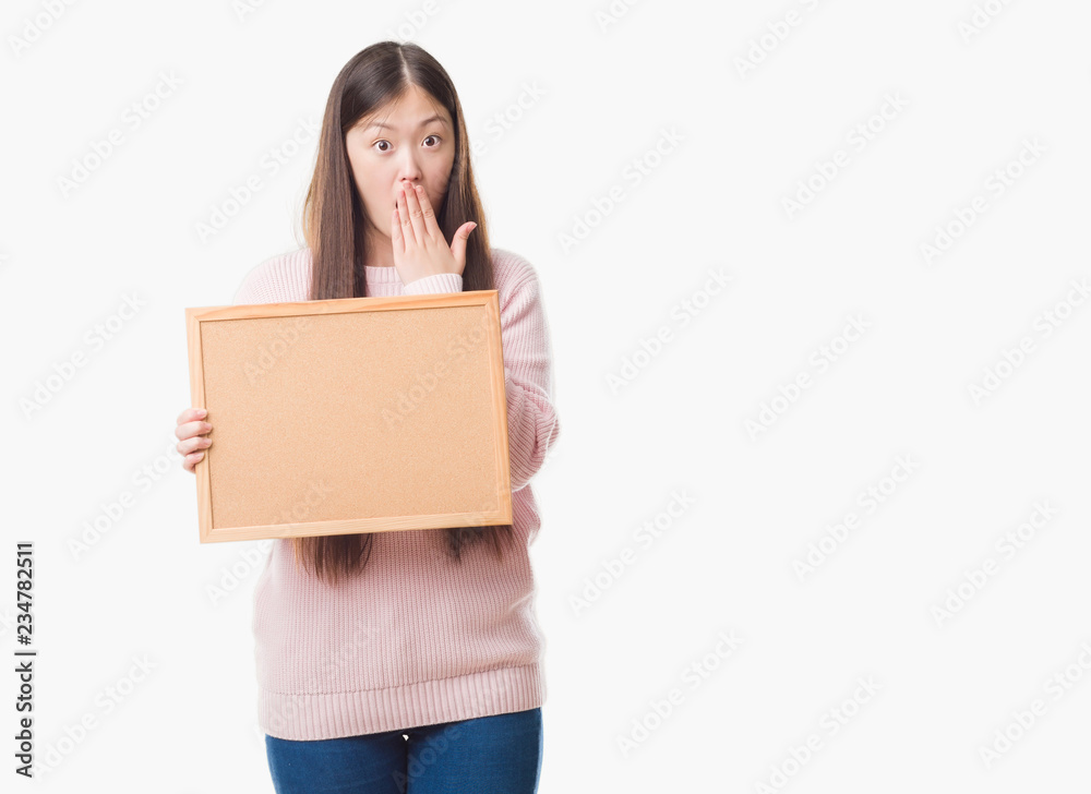 Young Chinese woman over isolated background holding corkboard cover mouth with hand shocked with shame for mistake, expression of fear, scared in silence, secret concept Young Chinese woman over isolated background holding corkboard cover mouth with hand shocked with shame for mistake, expression of fear, scared in silence, secret concept