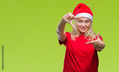 Young caucasian woman wearing christmas hat over isolated background smiling making frame with hands and fingers with happy face. Creativity and photography concept.