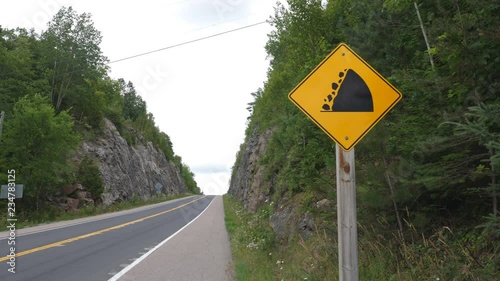 Yellow sign warning of falling rocks with rockcut and road ahead. Highway 35 near Miners Bay, Ontario, Canada. photo