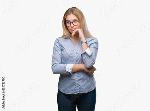 Young caucasian business woman wearing glasses over isolated background with hand on chin thinking about question, pensive expression. Smiling with thoughtful face. Doubt concept. © Krakenimages.com