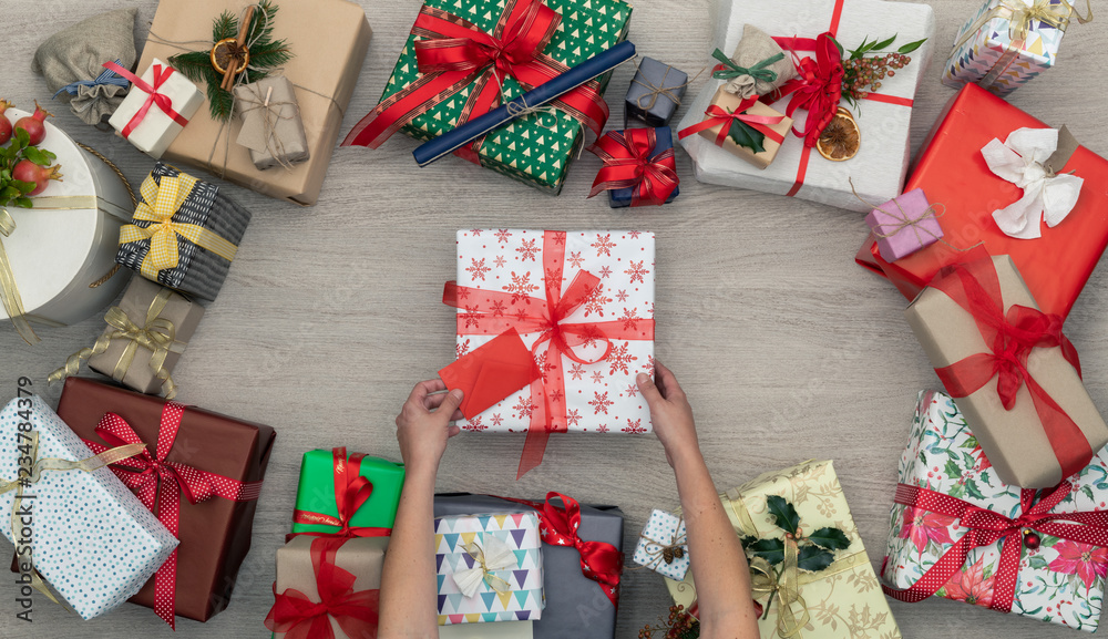 Obraz premium Hands with gift present box in vertical top view wooden table full of christmas or birthday gifts presents.Xmas winter holiday season party social media card background,portrait story