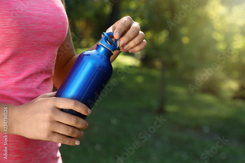 Young sporty woman with water bottle in park on sunny day, closeup. Space for text