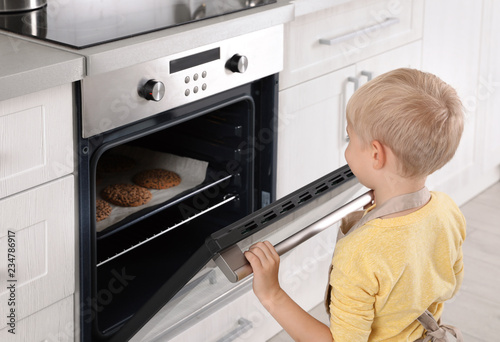 Little boy baking cookies in oven at home
