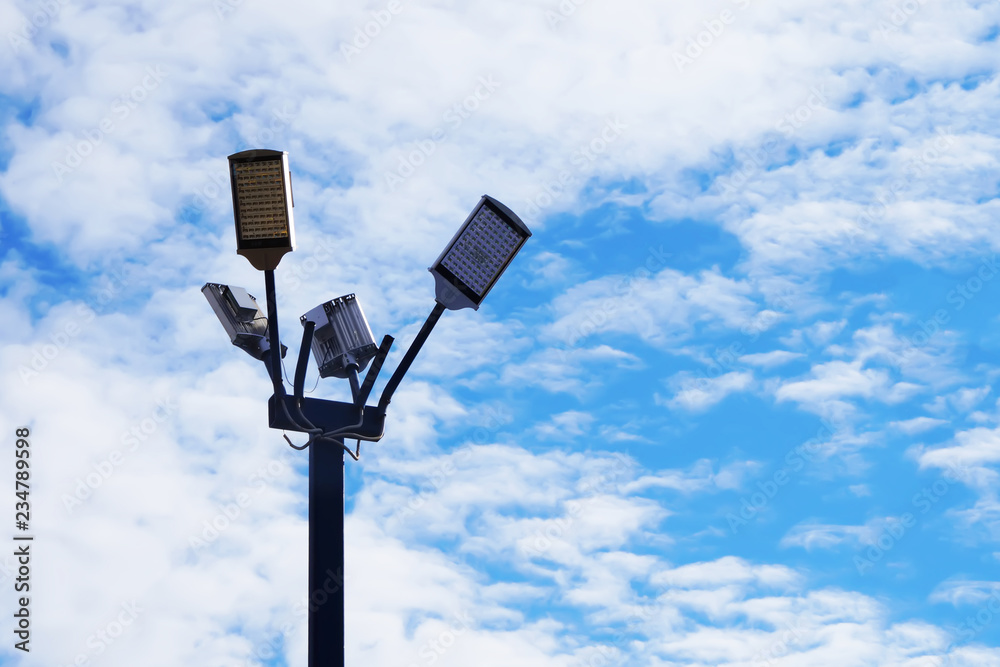 street mast of lighting with four lamps against the background of clouds and the blue sky. copy space street mast of lighting with four lamps against the background of clouds and the blue sky. copy space