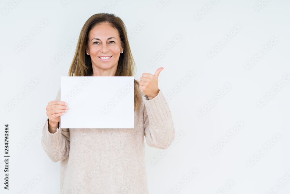 Middle age woman holding blank paper sheet over isolated background pointing and showing with thumb up to the side with happy face smiling Middle age woman holding blank paper sheet over isolated background pointing and showing with thumb up to the side with happy face smiling