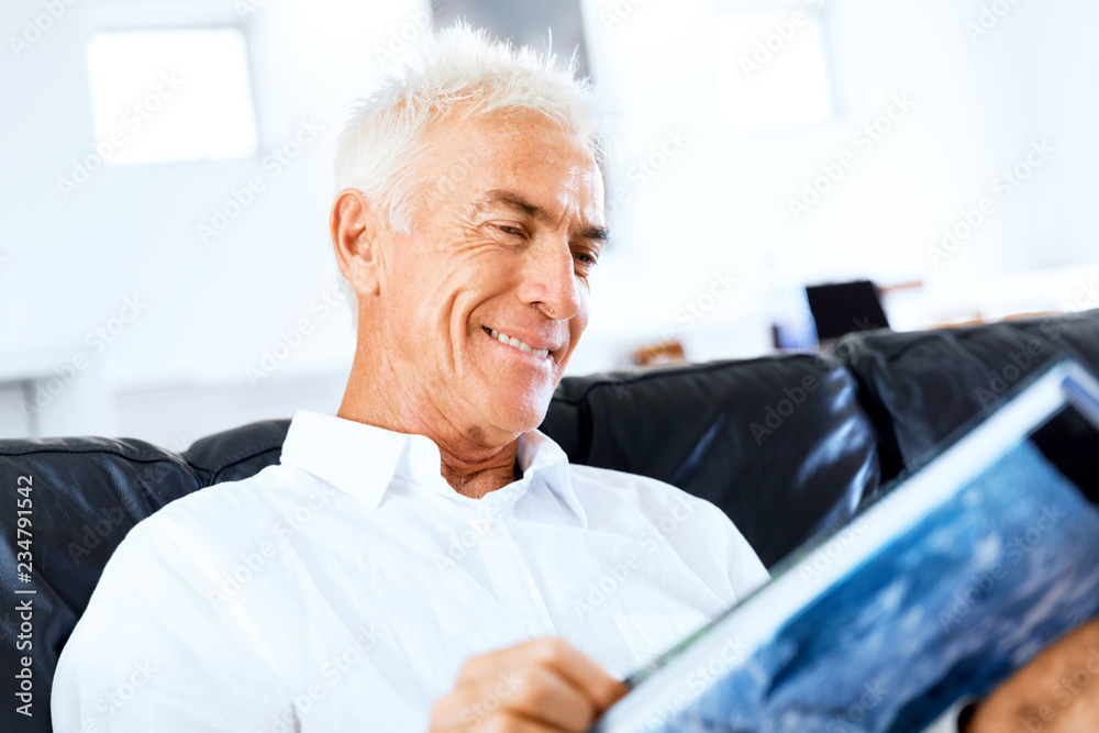 Handsome sennior man reading a book relaxing on a sofa