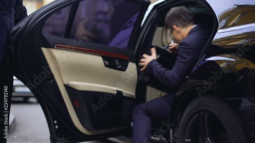 Personal driver opening backseat door in car for young successful businessman