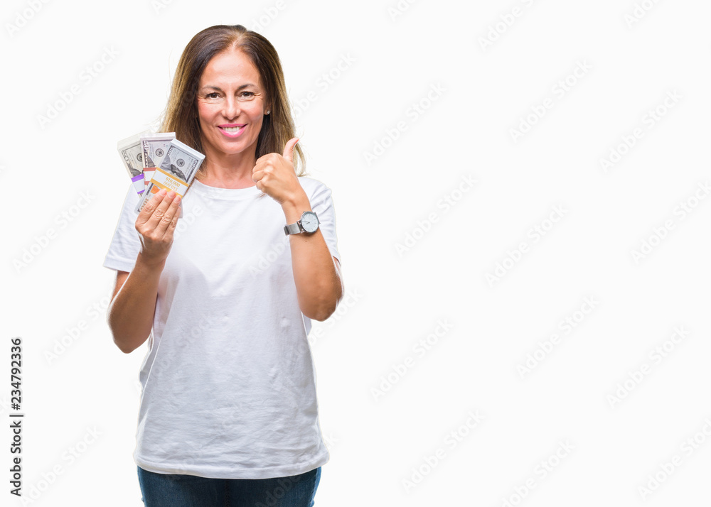 Middle age hispanic woman holding bunch of dollars over isolated background happy with big smile doing ok sign, thumb up with fingers, excellent sign Middle age hispanic woman holding bunch of dollars over isolated background happy with big smile doing ok sign, thumb up with fingers, excellent sign