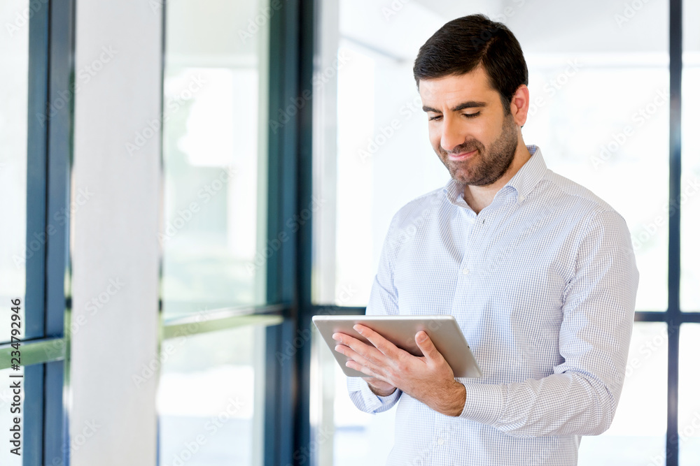 Young handsome businessman using his touchpad standing in office Young handsome businessman using his touchpad standing in office