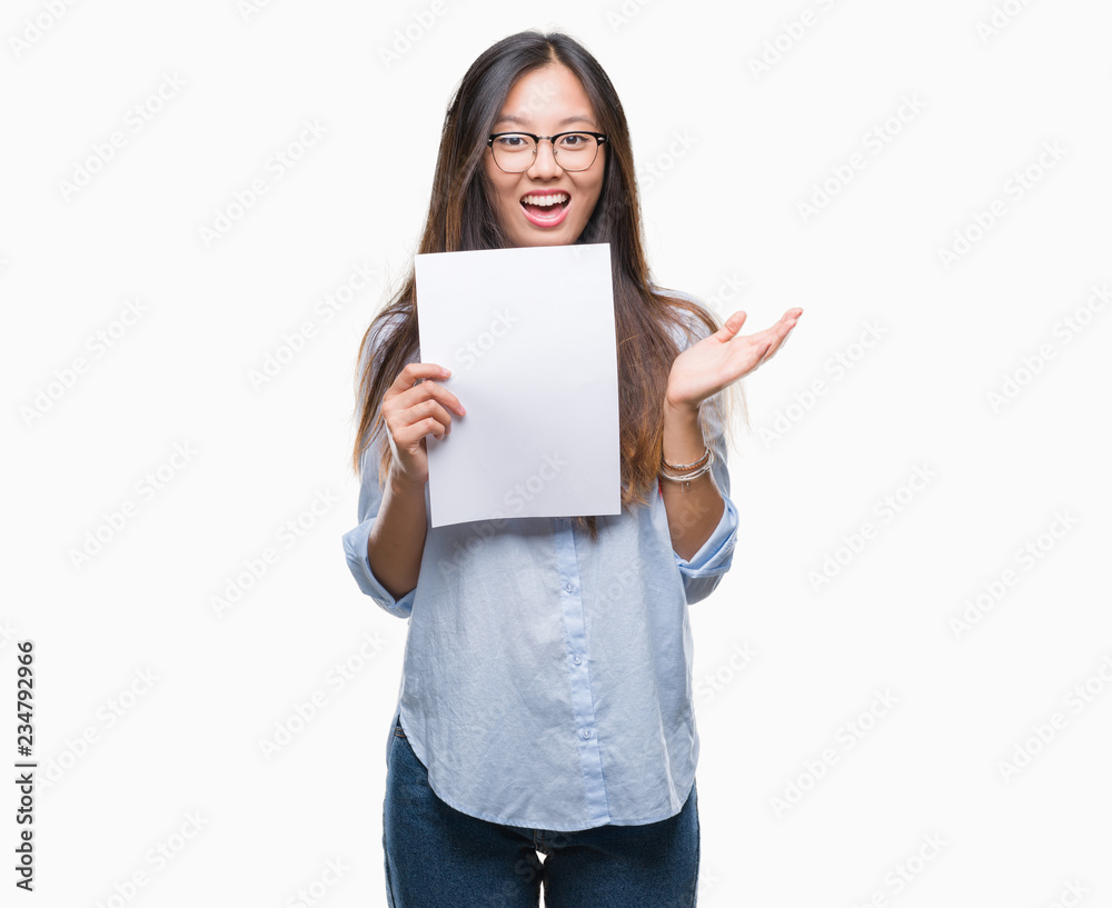 Young asian woman holding blank paper over isolated background very happy and excited, winner expression celebrating victory screaming with big smile and raised hands Young asian woman holding blank paper over isolated background very happy and excited, winner expression celebrating victory screaming with big smile and raised hands
