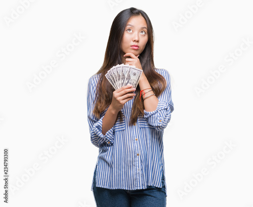 Foto Young asian woman holding dollars over isolated background serious face thinking