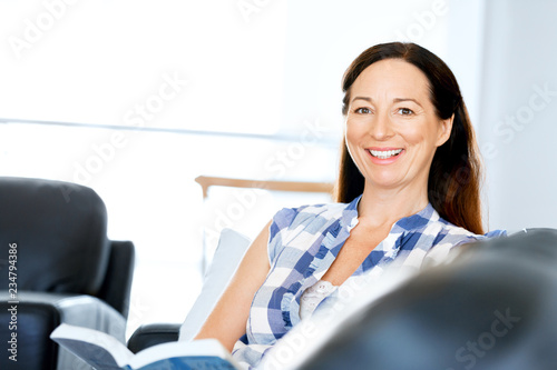 Happy woman reading a book relaxing on a sofa