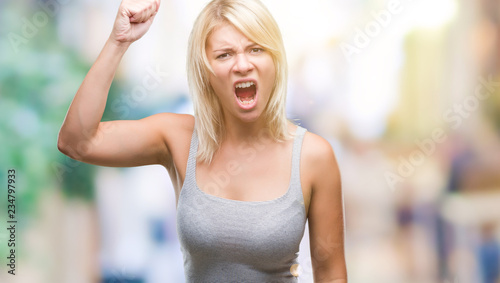 Young beautiful blonde woman over isolated background angry and mad raising fist frustrated and furious while shouting with anger. Rage and aggressive concept. © Krakenimages.com