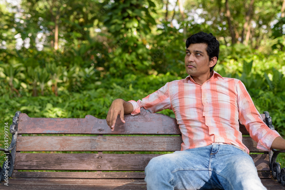 Obraz premium Indian man thinking while sitting on wooden bench in peaceful gr