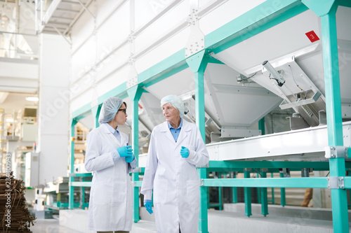 Portrait of two workers wearing white coat walking across clean production hall at modern factory  copy space