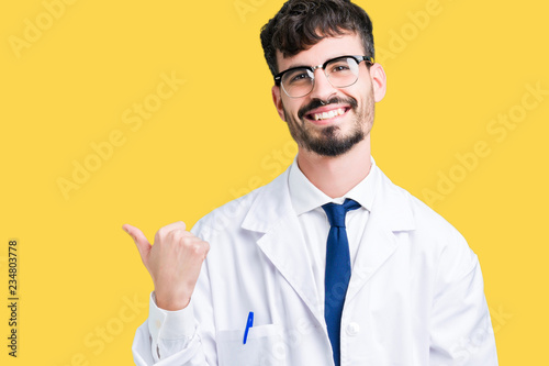 Young professional scientist man wearing white coat over isolated background smiling with happy face looking and pointing to the side with thumb up.