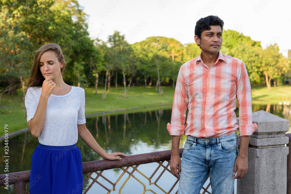 Multi ethnic couple thinking while looking sad on the bridge of Multi ethnic couple thinking while looking sad on the bridge of