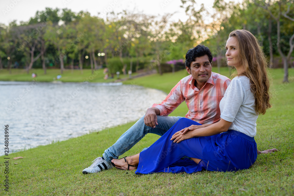Multi ethnic couple thinking while sitting in the meadow against Multi ethnic couple thinking while sitting in the meadow against