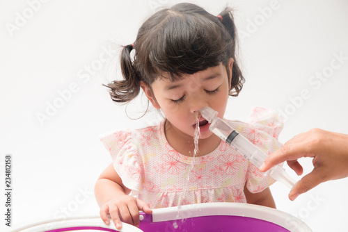 Asian mother making nasal wash for her baby girl by flushing kid'nose with syringe and saline. An Irrigation can benefit people who have sinus problems,nasal allergies isolated on white background photo