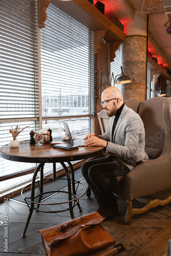 Portrait of young man with beard in the glasses looking to the monitor laptop. Successful people, businessman in comfortable cafe . Reading text during work on netbook