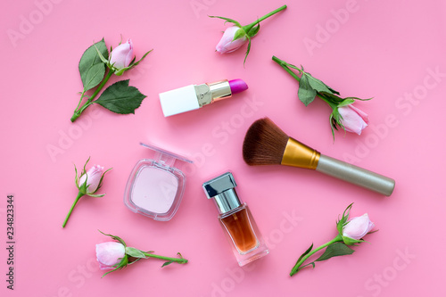 Makeup products for young girls. Composition with cosmetics with rose tones. Lipstick, bulk, eyeshadow, perfume, brushes and rose flowers on pink background top view