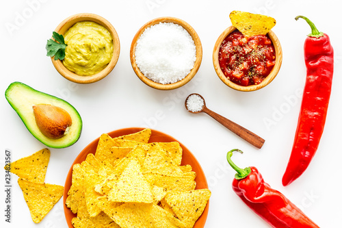 Popular mexican snack nachos. Tiangle nacho tortilla near salsa and guacamole sause, chili pepper, salt on white background top view photo