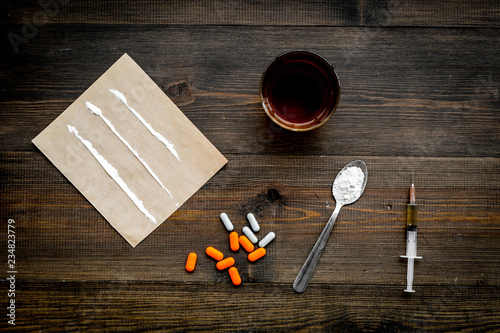 Take drugs, drugs addiction concept. White powder like heroine or cocaine, drug tracks pills, spoon, syringe on dark wooden background top view