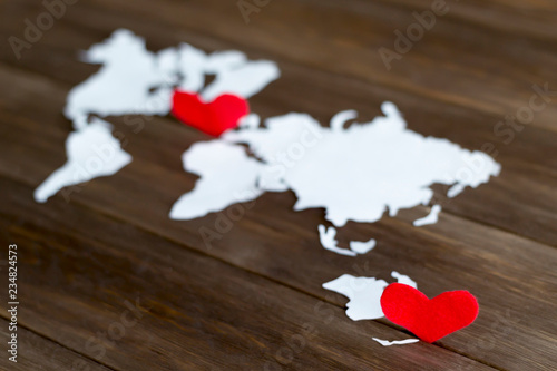 Two red felt hearts and world map cutted from white paper on the wooden background. Long-distance relationships concept. Close-up, soft focus, copy space, mock up, diagonal arrangement