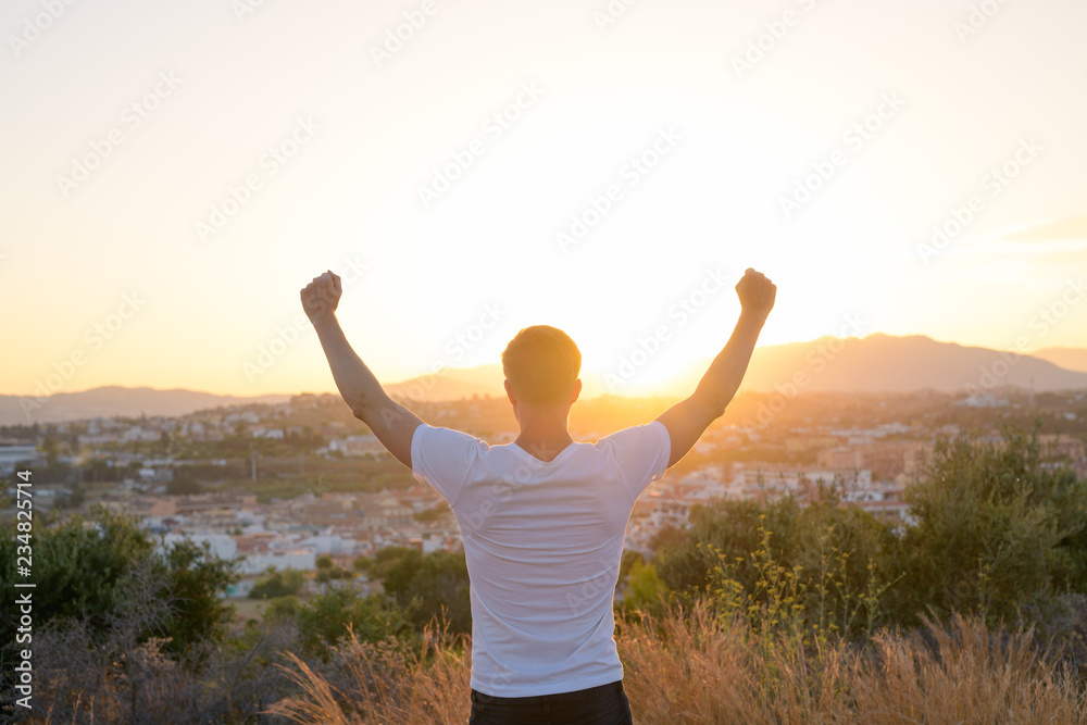 Rear View Of Happy Young Tourist Man Raising Arms On Top Of The Hill Rear View Of Happy Young Tourist Man Raising Arms On Top Of The Hill