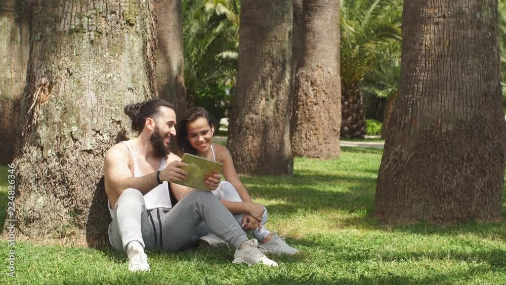 fitness, sport, technology and people healthy lifestyle concept - cheerful caucasian couple in sportswear with tablet pc computer outdoors in green park area fitness, sport, technology and people healthy lifestyle concept - cheerful caucasian couple in sportswear with tablet pc computer outdoors in green park area