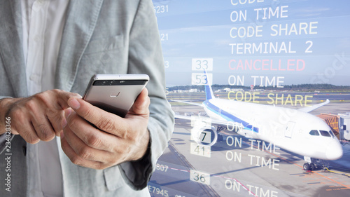 Businessman with mobile phone in international airport checking at the flight information board for boarding gate
