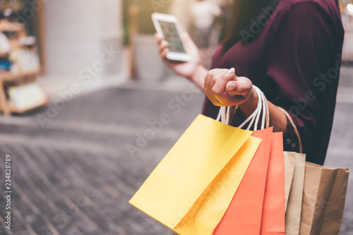 Consumerism, shopping, lifestyle concept, Young woman holding colorful shopping bags and smartphone enjoying in shopping