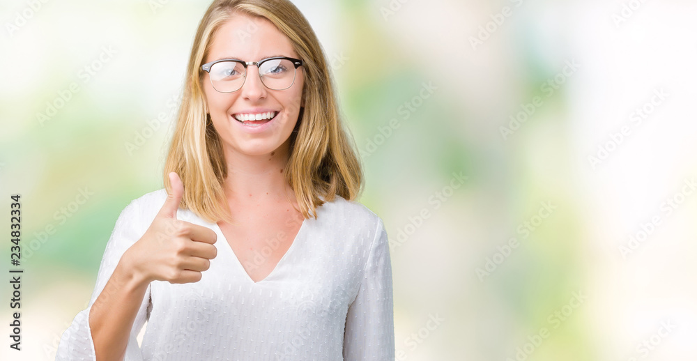 Beautiful young woman wearing glasses over isolated background doing happy thumbs up gesture with hand. Approving expression looking at the camera with showing success.