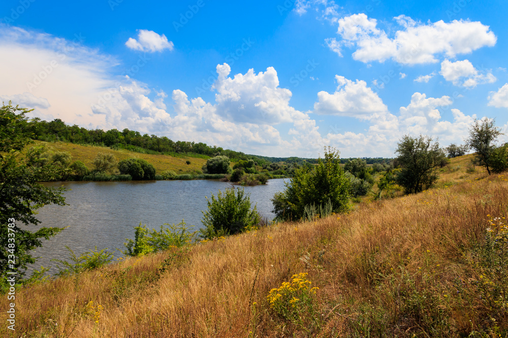 Summer landscape with beautiful lake, green meadows, hills, trees and blue sky Summer landscape with beautiful lake, green meadows, hills, trees and blue sky
