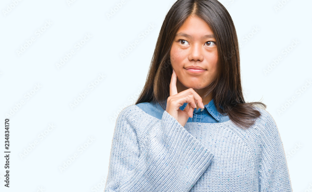 Young asian woman wearing winter sweater over isolated background with hand on chin thinking about question, pensive expression. Smiling with thoughtful face. Doubt concept. Young asian woman wearing winter sweater over isolated background with hand on chin thinking about question, pensive expression. Smiling with thoughtful face. Doubt concept.