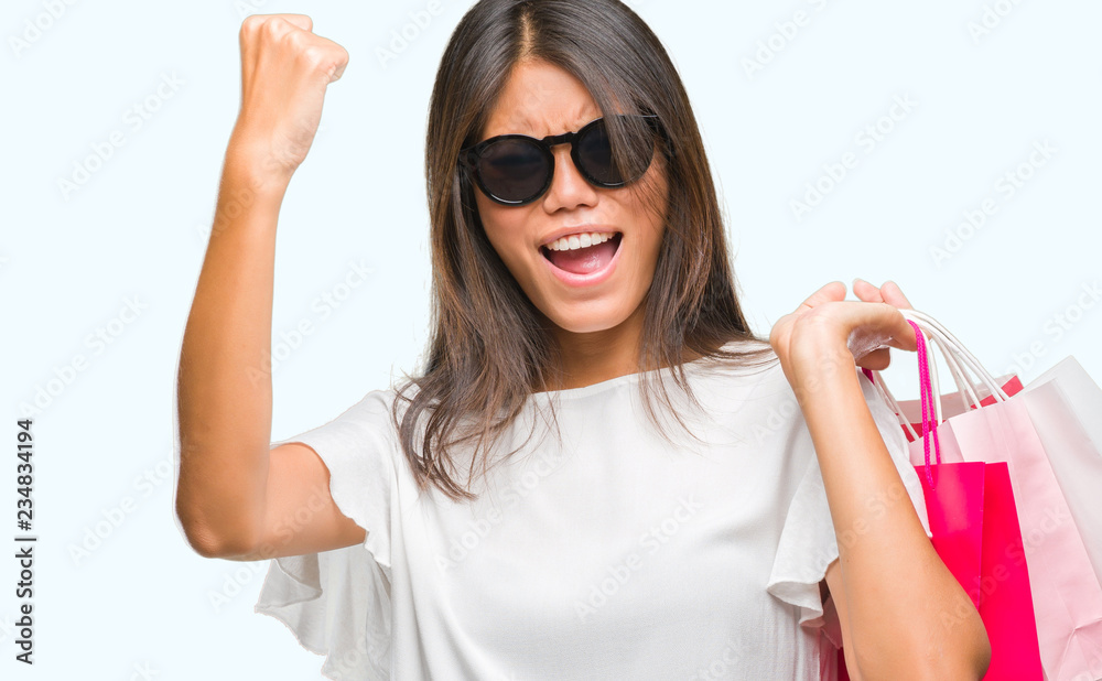 Young asian woman holding shopping bags on sales over isolated background annoyed and frustrated shouting with anger, crazy and yelling with raised hand, anger concept