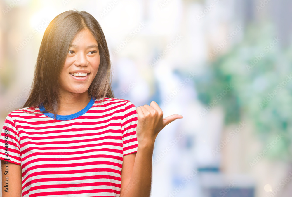 Young asian woman over isolated background smiling with happy face looking and pointing to the side with thumb up.